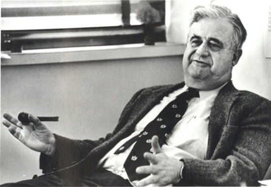 Marshall N. Rosenbluth, talking, leaning back in chair at desk, with pipe
